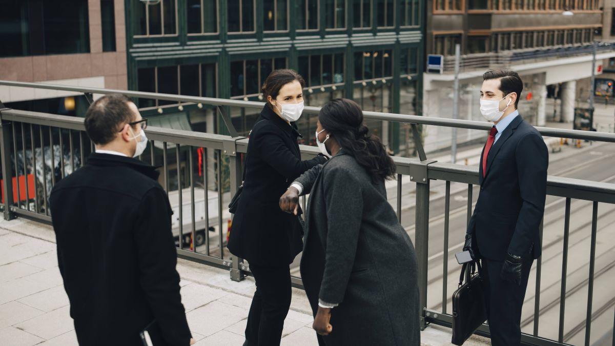 Female entrepreneurs doing elbow bump while standing with male colleagues on bridge in city during pandemic