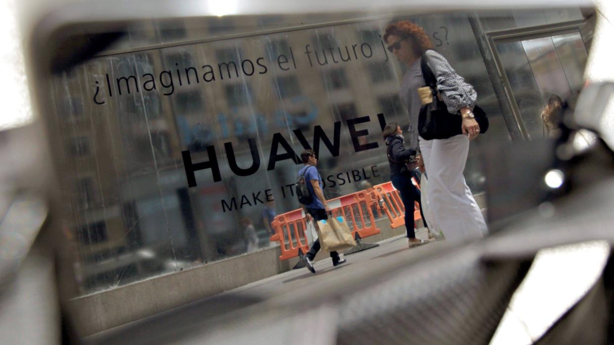 Photo of several passers-by walking past a Huawei store reflected in a mobile phone in Madrid, Spain