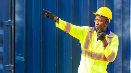 Bild: Ein Arbeiter in gelber Kleidung vor einem Schiffscontainer