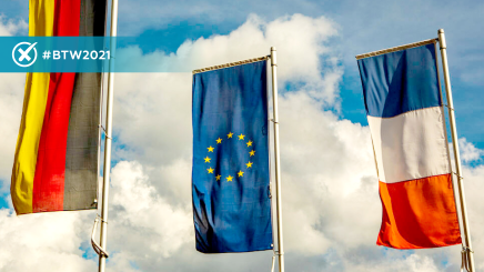 Photo of German, EU and French flags waving in a blue sky