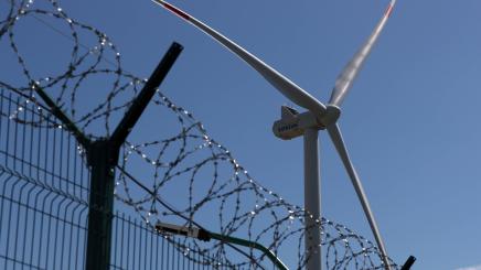A wind turbine is seen behind a barbed wire fence